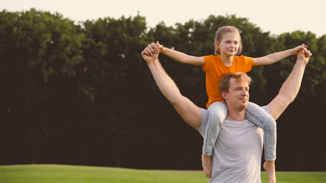 joyful father carrying his happy daughter on shoulders and spinning around in a park