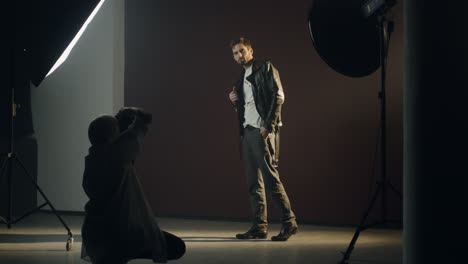 joven caucásico con estilo posando para la cámara de la fotógrafa en un estudio oscuro durante la sesión de fotos