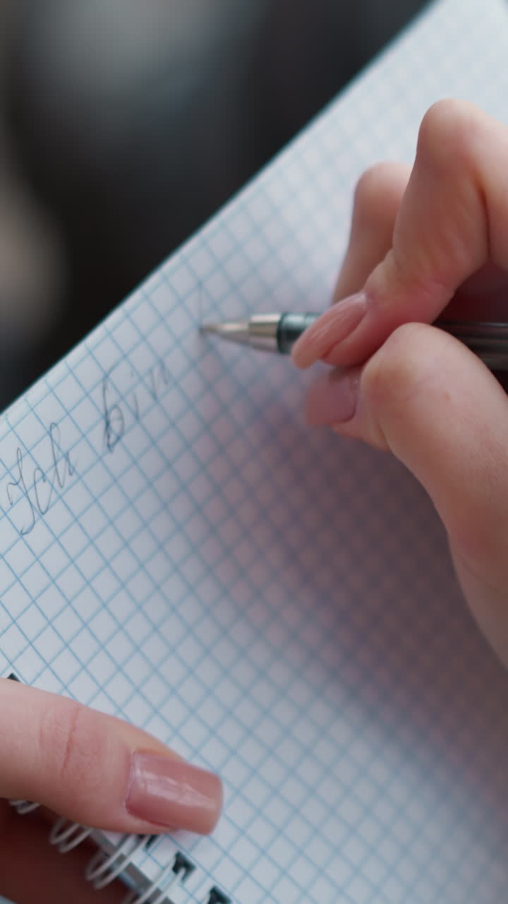 vista de cerca de la mano de una mujer escribiendo en un cuaderno con pluma, centrándose en los dedos y la pluma en papel gráfico, primer plano detallado del proceso de escritura, la mano femenina mostrando una técnica de escritura graciosa