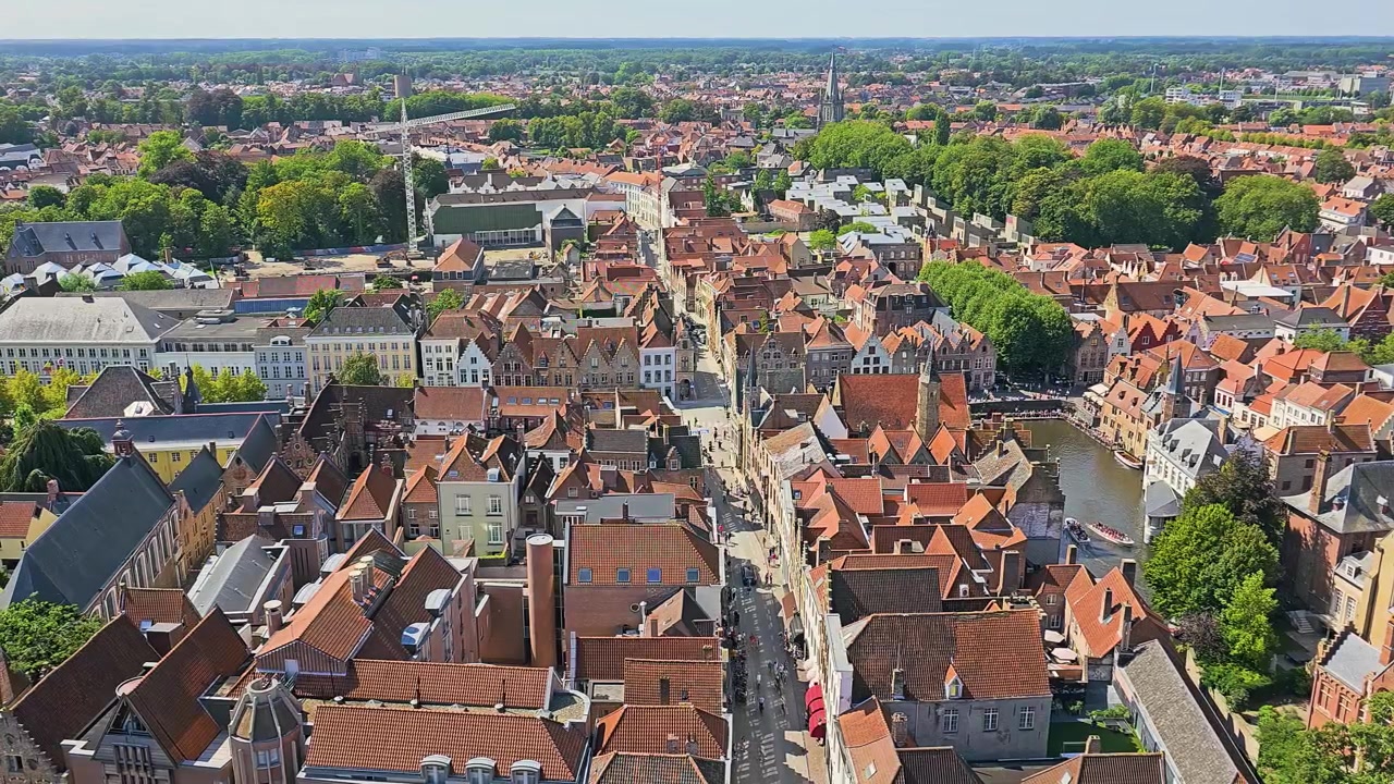 Brugges, Belgiens skyline set ovenfra med røde tegltage, historisk kirketårn, gamle bystræder, traditionelle flamske bygninger, grønne træer og solrigt rejselandskab om sommeren.