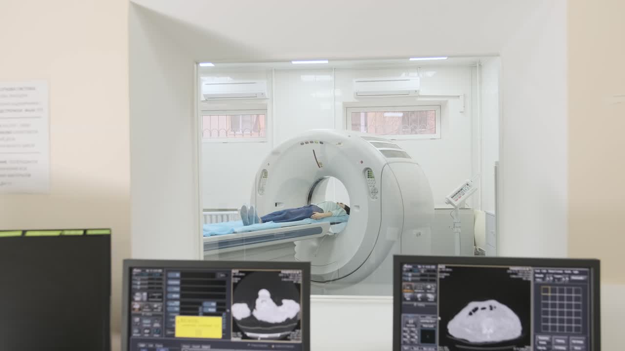 dos radiólogos calificados examinan a una paciente femenina que está acostada bajo un escáner de ct o mri. pantalla de computadora con imagen de diagnóstico de resultado. vista a través de una ventana de vidrio en una clínica moderna.