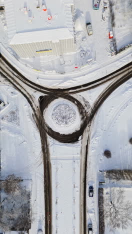 Vertical drone shot above traffic in a snowy city roundabout, sunny, winter day