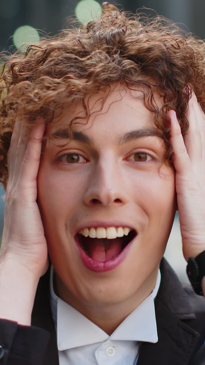 Businessman looking at camera shocked by sudden victory game winning good news outside office