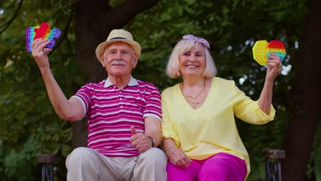 Senior-stylish-grandmother-grandfather-showing-squeezing-anti-stress-push-pop-it-popular-toy-game