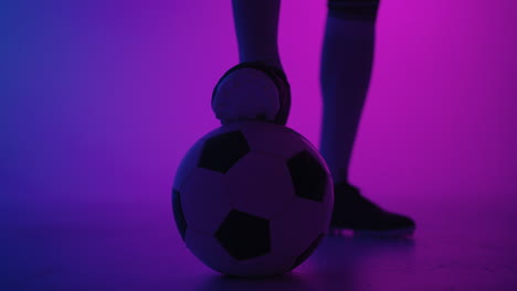 close-up of the foot of a professional black football player standing on the ball in slow motion in the blue-red neon light of the studio. brazilian football player foot on the ball to pose