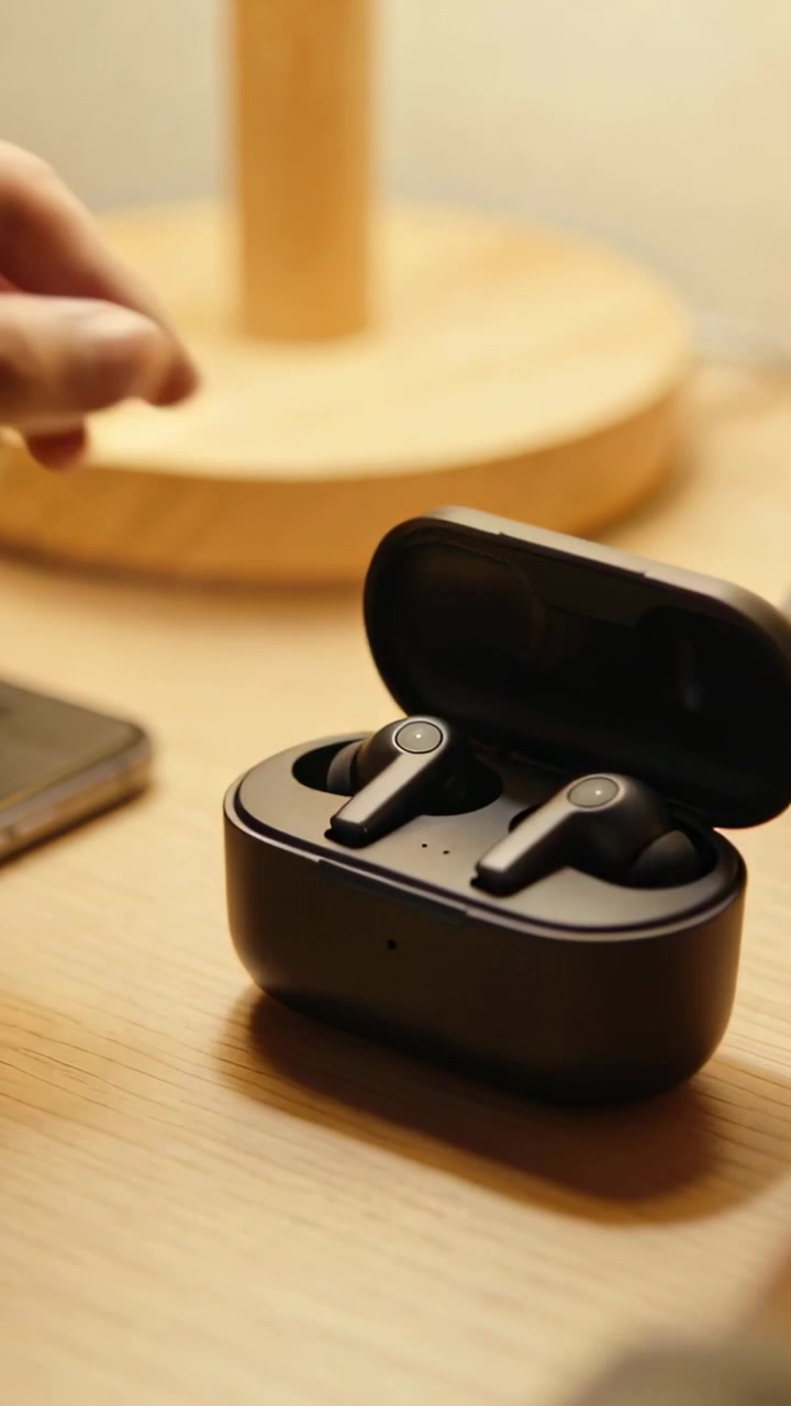 Video verticale: Mani che sollevano e aprono la custodia degli auricolari sulla scrivania di casa, controllando i contatti vicino a una lampada da telefono