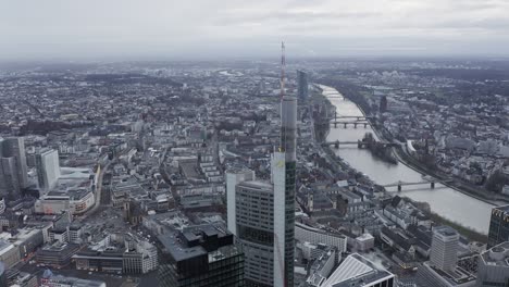 aerial descending view of commerzbank tower and cityscape. several bridges spanning river winding through town. frankfurt am main, germany