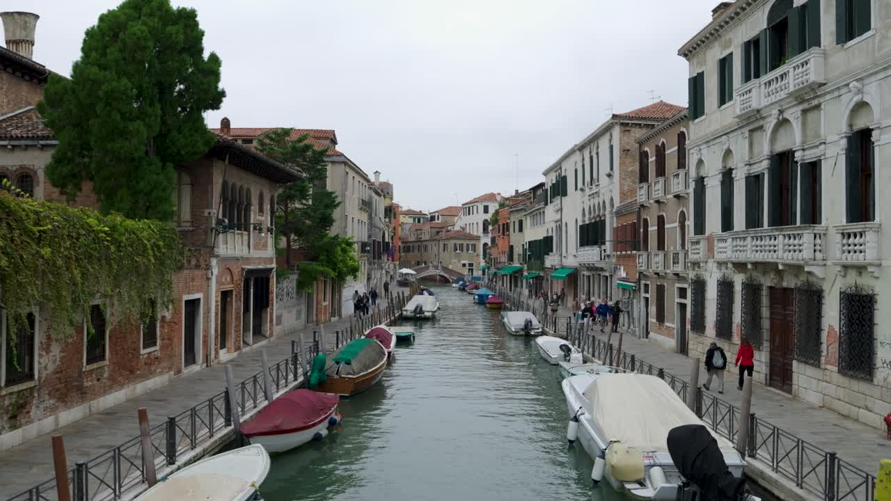 Typical small canal street in Venice with few tourists on cloudy autumn day