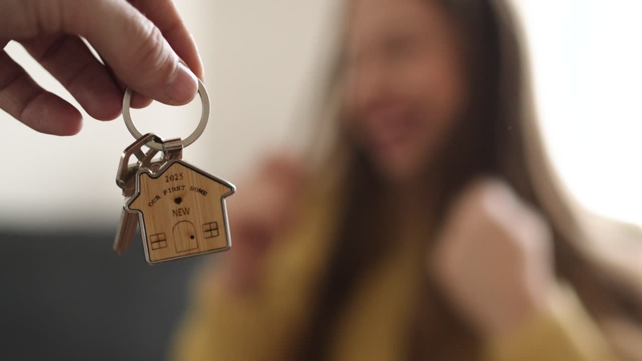 Una mano porge la chiave della sua nuova casa, mentre la donna reagisce con puro entusiasmo. La chiave è a fuoco, a simboleggiare una pietra miliare di gioia e l'emozione di un nuovo inizio.