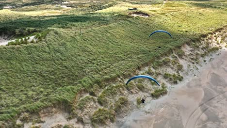 Thrilling-dune-soaring-by-two-paragliders-along-Langevelderslag-coastline,-drone