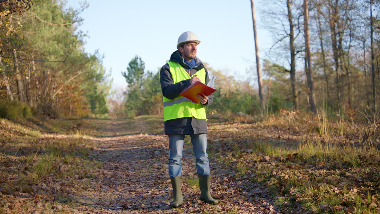 ingeniero masculino abriendo sus notas en su tablón de recortes y escribiendo en él mientras estaba en el medio del bosque, de mano
