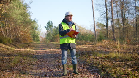 male engineer opening his notes on his clipboard and writing on it while in the middle of the forest, handheld