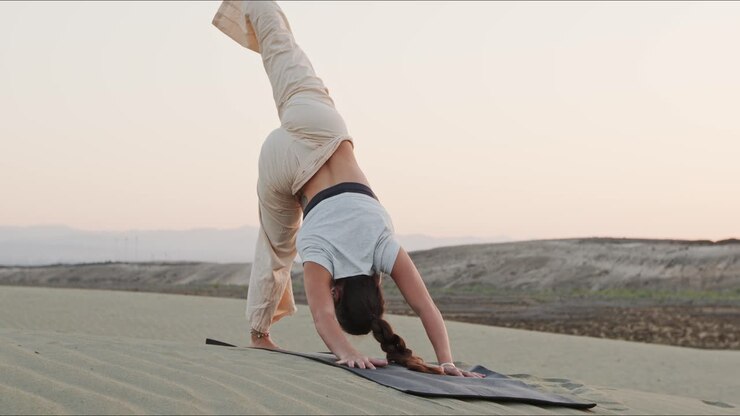 Giovane istruttrice di yoga bruna su una duna di sabbia che esegue una routine yoga al mattino presto
