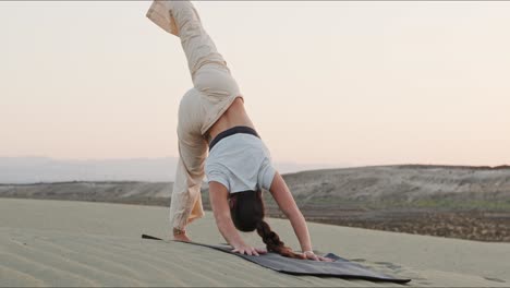 young brunette yoga instructor on a sand hill performing a yoga routine early in the morning