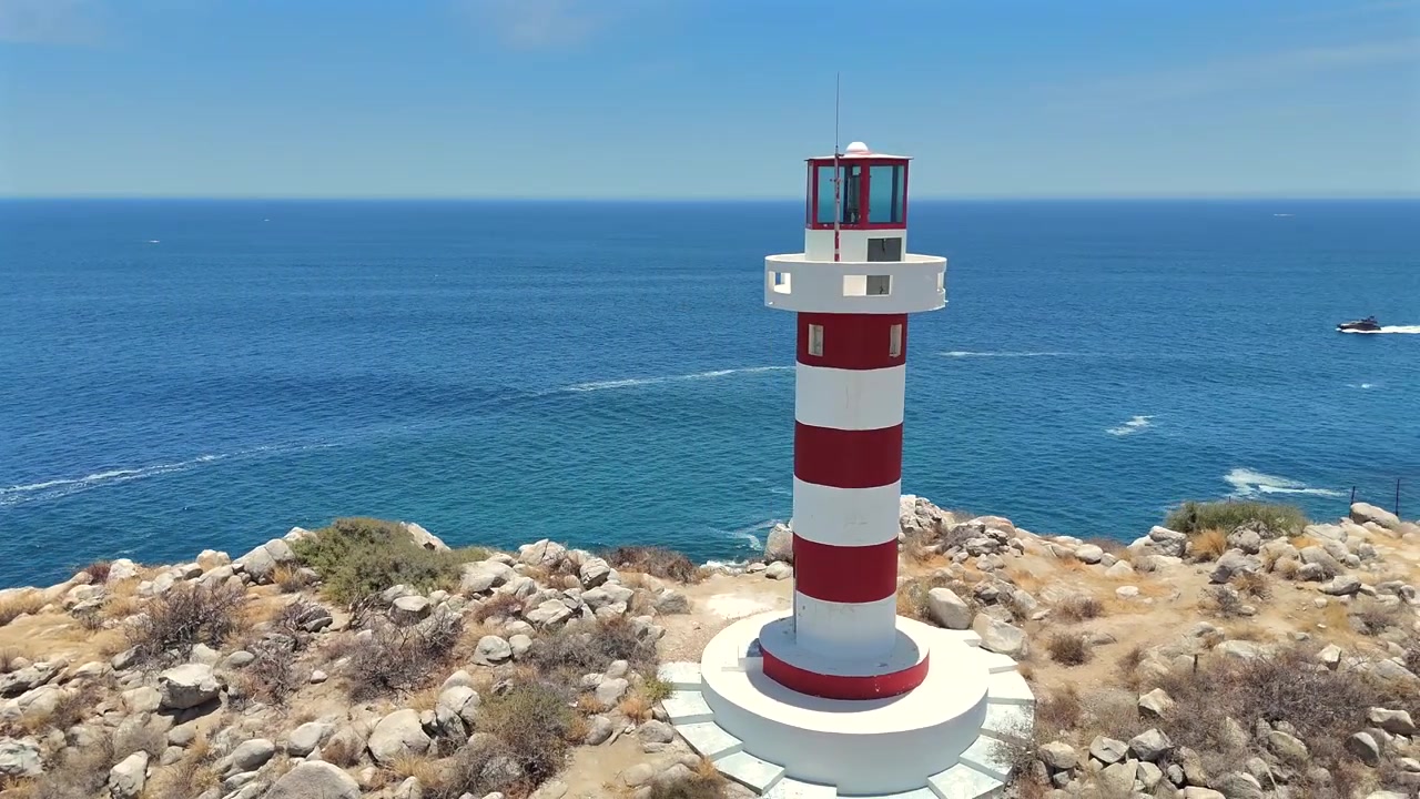 Drone orbita il Faro El Encanto a Cabo San Lucas, iniziando con la vista della spiaggia e della costa e ruotando per rivelare l'oceano aperto che si estende oltre.