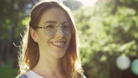 close-up view of a caucasian woman in glasses looking and smiling at camera in the park on a summer day