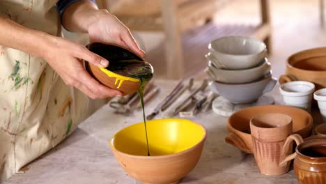 Mid-section-of-female-potter-pouring-paint-into-bowl