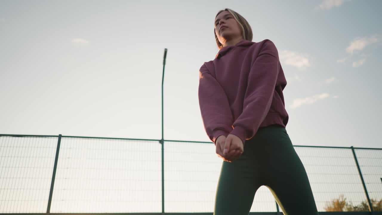 vista hacia arriba de una joven con leggings verdes jugando al voleibol, el fondo presenta una valla de red y un campo abierto, con el sol brillando brillantemente