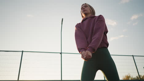 upward view of young lady in green leggings playing volleyball, background features net fence and open field, with the sun shining brightly