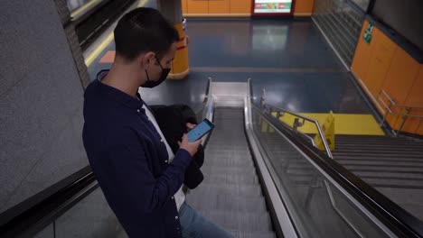 unrecognizable man surfing internet on smartphone on escalator in underground