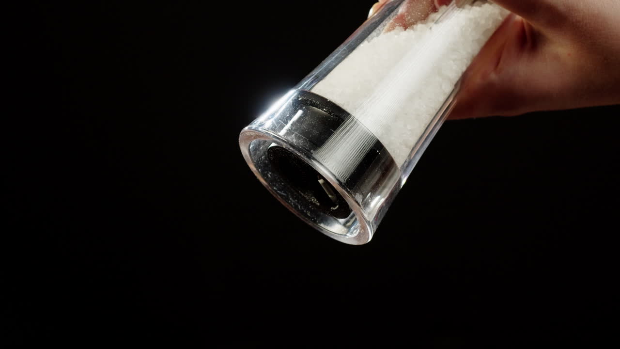 Primer plano de una mano moliendo sal de un molinillo transparente.