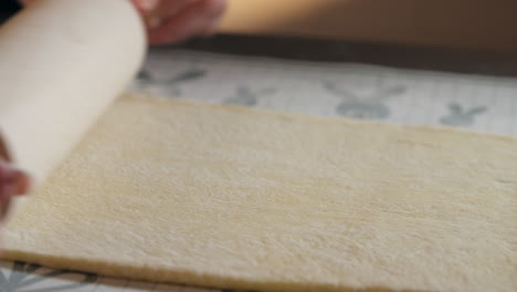 flattening dough with rolling pin. making cinnamon roll. closeup shot