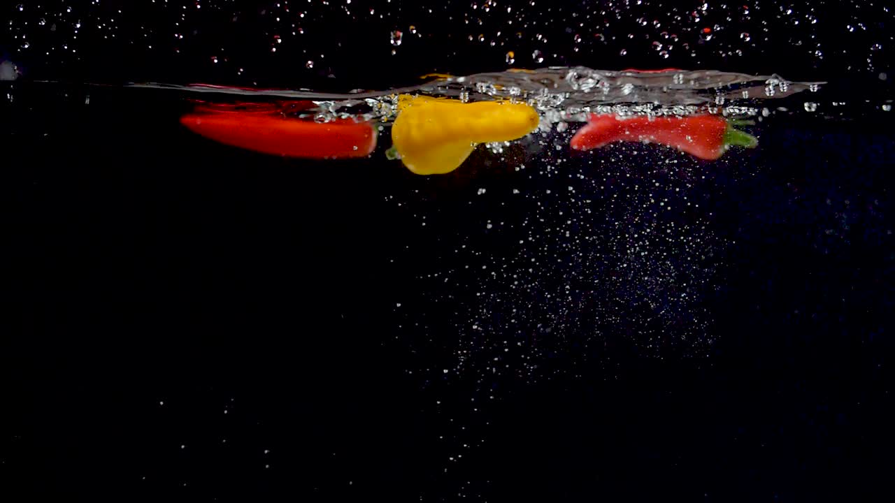 활기찬 노란색 달콤한 고추가 슬로우 모션으로 물에 떨어지고 있습니다.