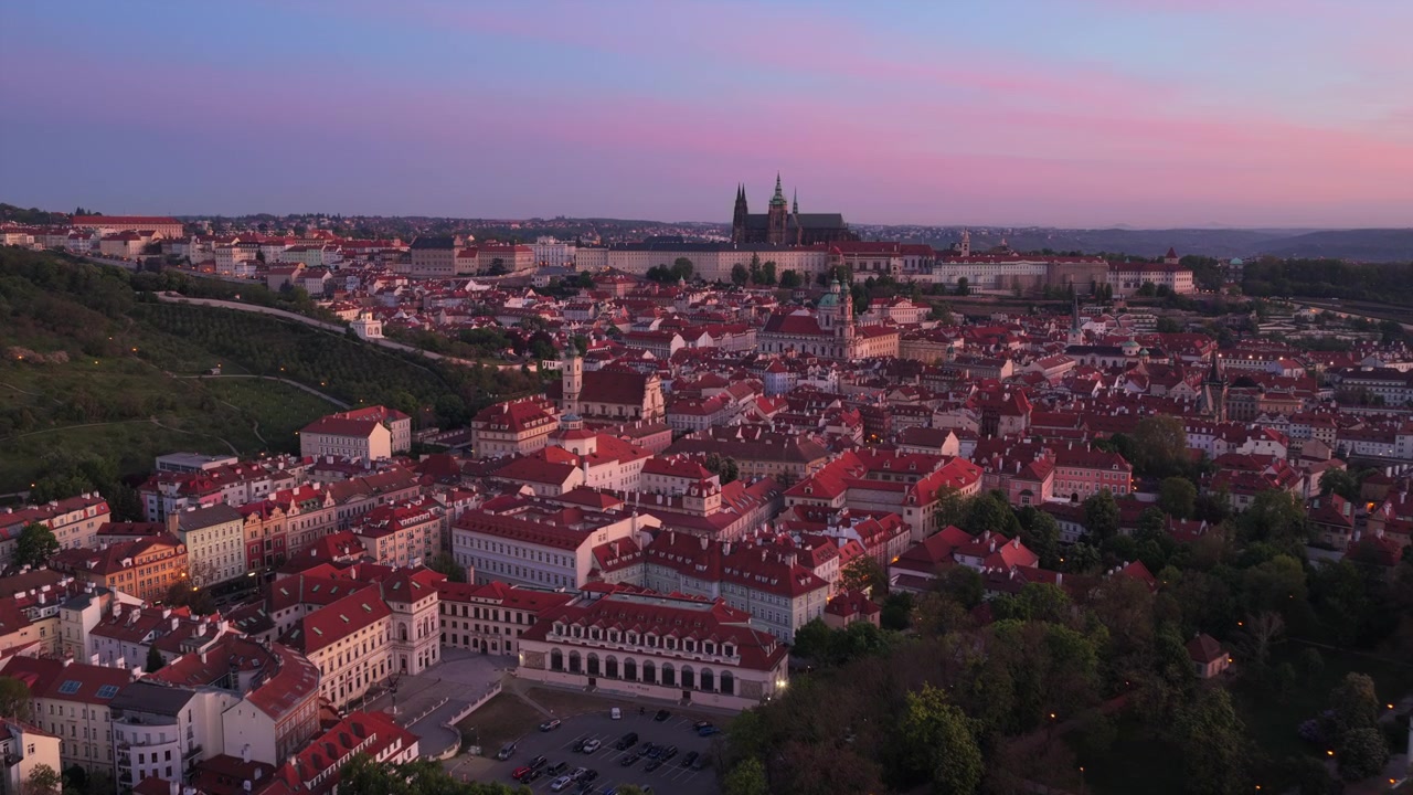 Vista aérea de drone ao amanhecer rosa-púrpura do distrito do Castelo de Praga e Malá Strana, com telhados densos de telhas vermelhas e as torres da Catedral de São Vito elevando-se acima, Praga, República Tcheca