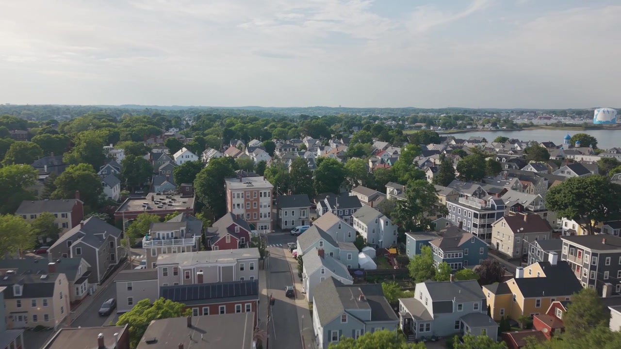 Historiske kolonihus samlet blant tett trekronetak, et gult herskapshus med kledning som forankrer en trekantet gate nær et fjernt kirketårn i Salem, Massachusetts om sommeren. Luftfoto med drone.