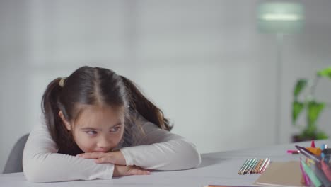 studio shot of bored hyperactive girl sitting at table at home with colouring pencils