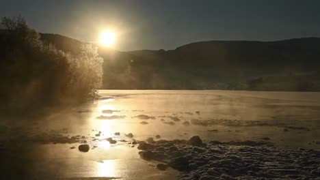 Frozen-misty-river-at-sunset-with-silhouette-mountain,-Voss-Norway