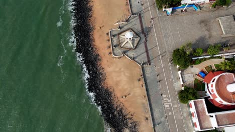 early morning aerial footage of puducherry's coastline highlights the mahatma gandhi statue, a prominent lighthouse, and the famous rock beach, with waves from the bay of bengal gently rolling in
