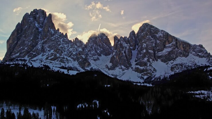 Drammatica catena montuosa innevata stagliata contro un bellissimo tramonto con nuvole, che crea una suggestiva scena crepuscolare