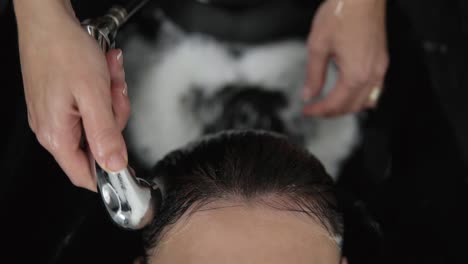 close-up professional hairdresser hands washes hair woman client in a beauty salon, she pours water on her head. proffesional movements. footage from the top