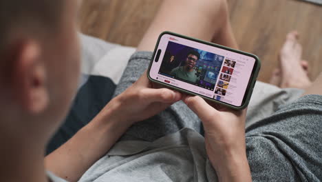 teenager watching a youtube video on a smartphone while lying in bed.