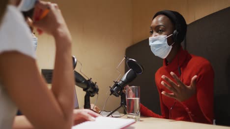 three diverse female radio hosts wearing face masks talking on microphone for radio podcast