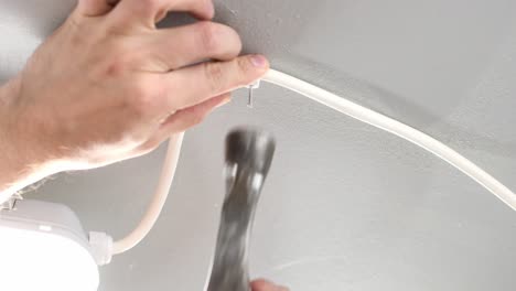 white male nailing white cord to roof ceiling with old hammer