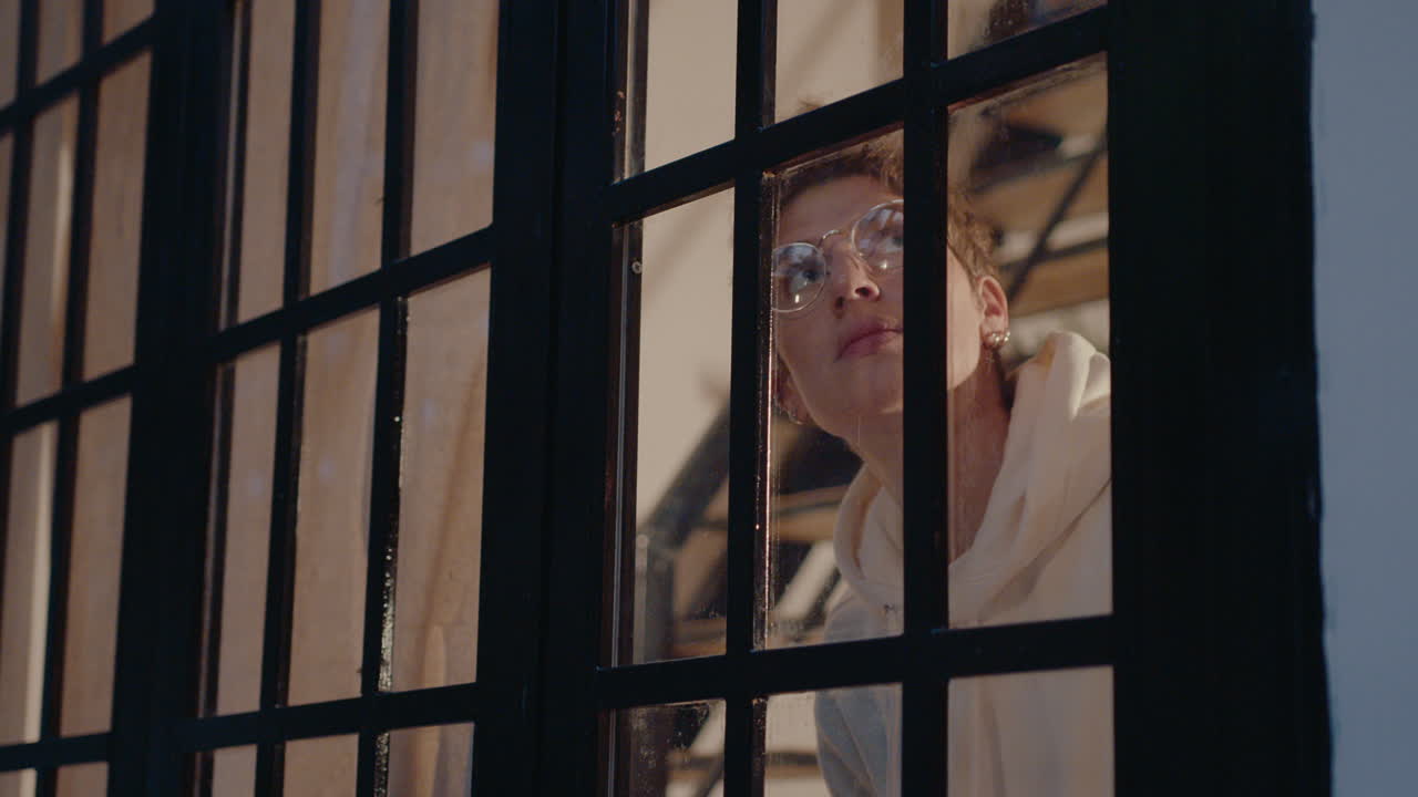 Young Woman Looking through Window and Closing Curtain