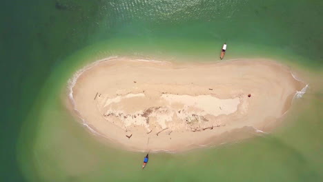 vista de drones de una pequeña isla celestial con agua azul-verde alrededor y 2 botes tailandeses tradicionales estacionados en la orilla