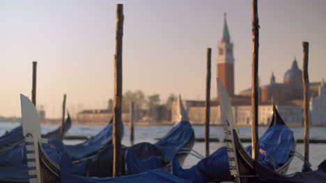 a closeup of covered gondolas swaying on a pier against the blurred venice view