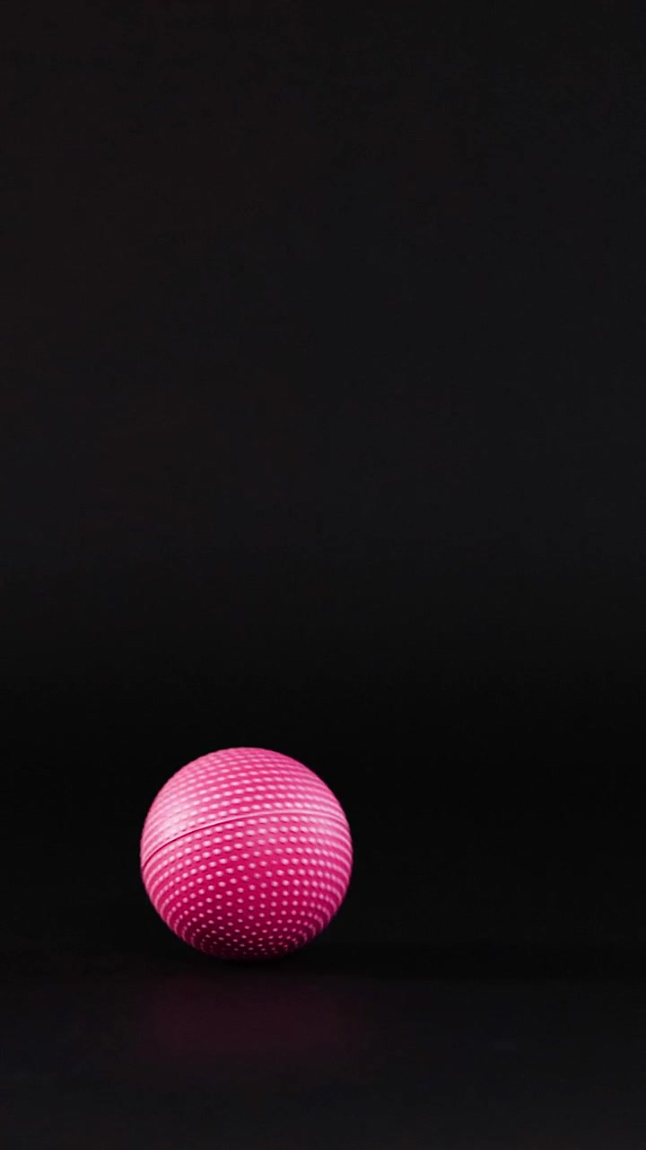 A pink ball rolls across a dark surface