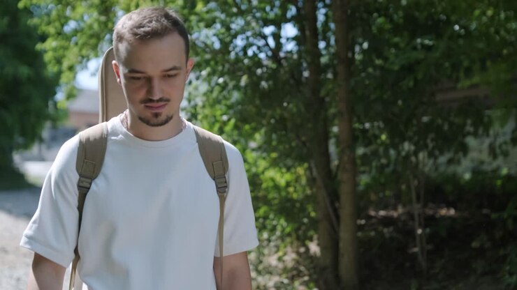 Young Man Walking with Guitar on Street Near Forest