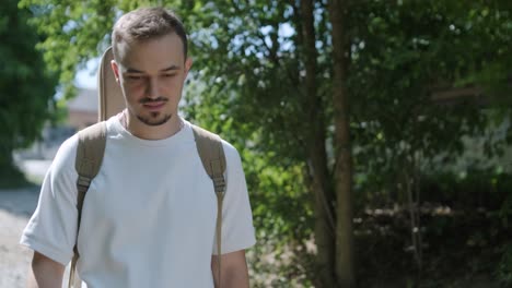 young man walking with guitar on street near forest