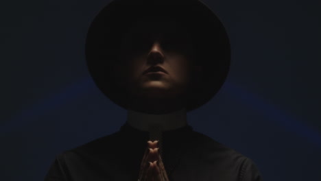 praying man in priest costume posing in dark studio
