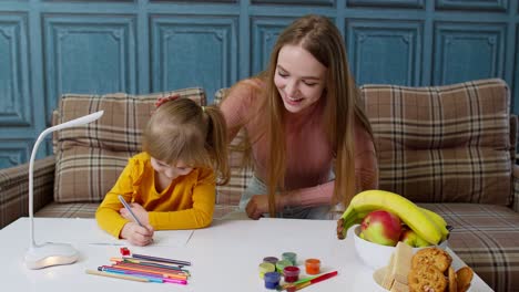 Lovely-mother-babysitter-teacher-helping-kid-daughter-with-homework,-learning-writing-at-home