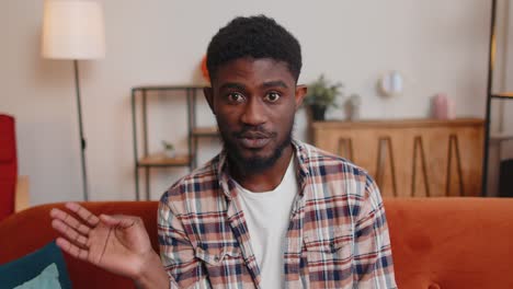 man sitting on home sofa, looking at camera, making video conference call with friends or parents
