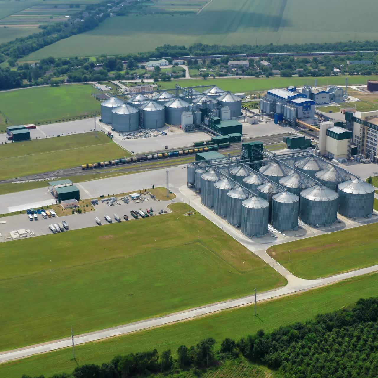 Agricultural industry. Modern factory on green field with steel elevators. Industrial buildings and granary under blue sky. Aerial view