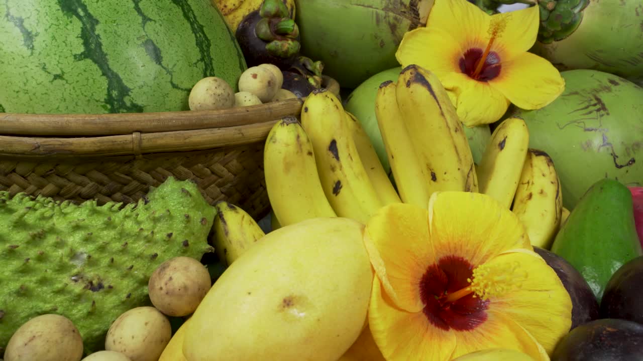 This captivating image showcases an assortment of tropical fruits commonly found in Asia, beautifully arranged with a vibrant hibiscus flower as a centerpiece.