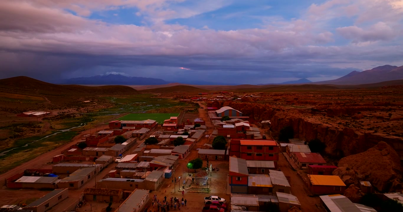 Aldeia remota de Aguas Calientes no Altiplano Boliviano sob um pôr do sol tempestuoso dramático e colorido. Vista aérea frontal, espaço para texto.