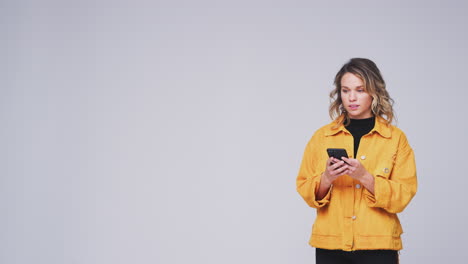 Studio-Shot-Of-Woman-Against-White-Background-Sending-Text-Message-On-Mobile-Phone-In-Slow-Motion